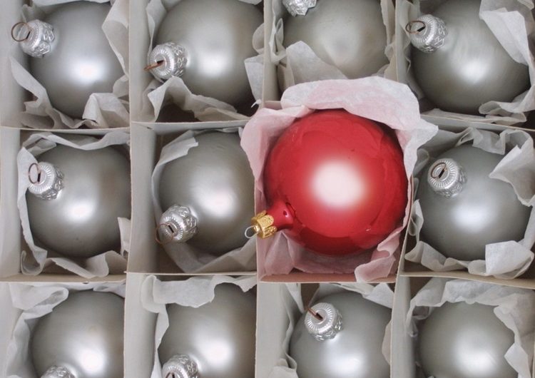 Imagen de bolas de navidad color plata ordenadas dentro de una caja y una bola de navidad roja en una de las líneas